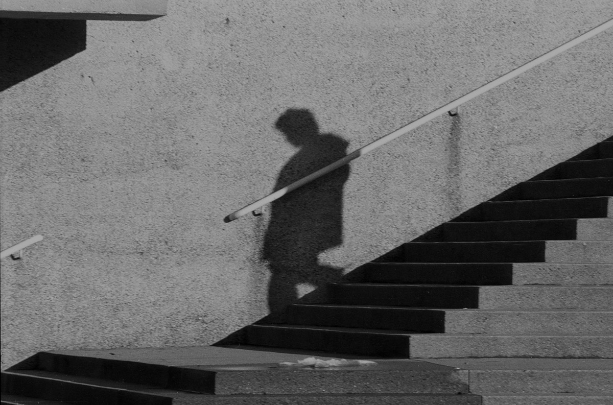 Black & White photograph of a man's shadow descending a concrete outdoor staircase. 